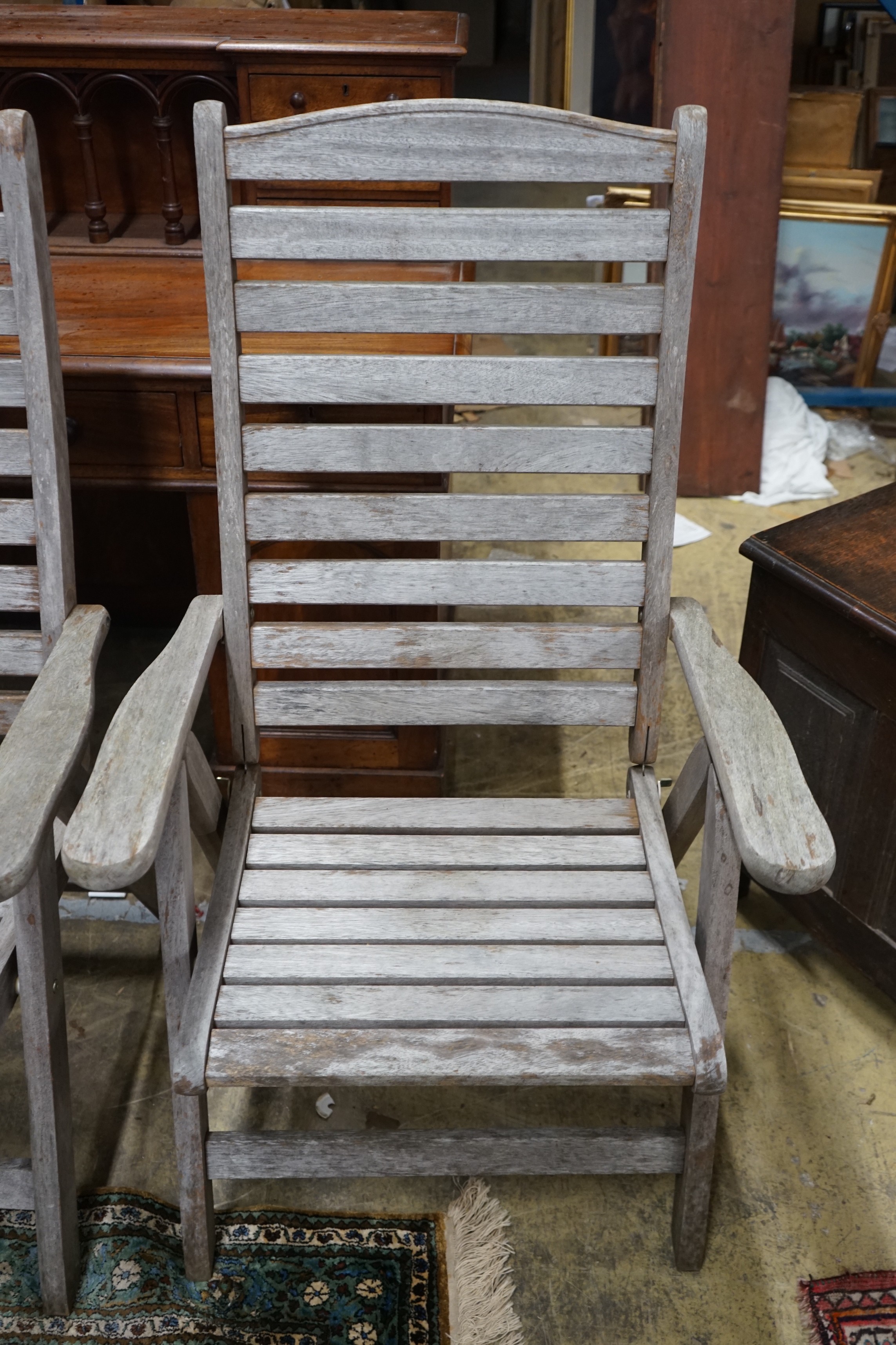 A pair of weathered teak folding garden armchairs, height 112cm